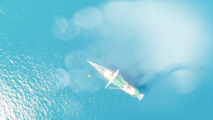 Bird's eye view of a sailing ship on the light blue water surface.
