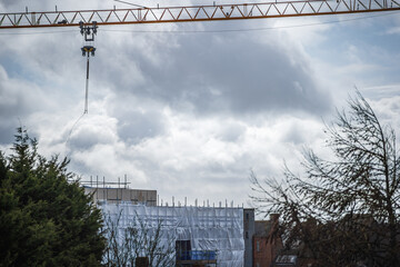 Construction crane above flame retardant scaffold sheeting wrapped apartments building during insulation in england uk - obrazy, fototapety, plakaty