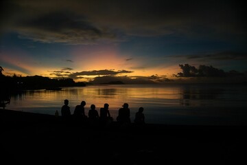 Silhouette of people looking at the calm coast during sunset