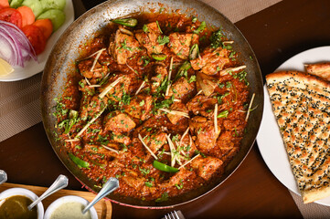 Spicy chicken karahi in the wide steel bowl topped with green chilli and ginger and served with garlic naan - obrazy, fototapety, plakaty