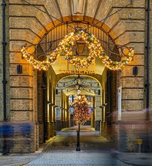 Vertical shot of a stone arch gate with illuminating Christmas lights hanging in the street