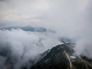 Aerial view of a dense green mountain forest covered with dense fog on a cloudy day