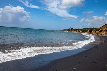 Wavy sea with a black sand beach under a cloudy sky