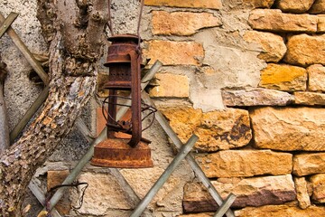 Old rusty lantern on a leafless tree in front of a sandstone wall in daylight