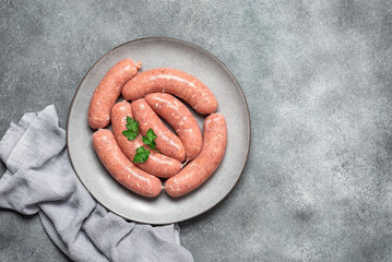 Raw homemade sausages close-up in a plate on a gray concrete background. Top view, flat lay, copy space.