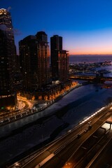 Vertical shot of the frozen river alongside the tall skyscrapers during the sunrise