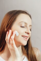 Young smiling woman is applying cream to her cheeks