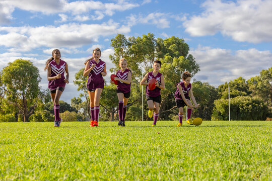 five children in football uniforms running towards the camera on green grass
