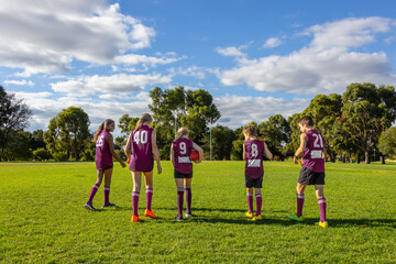 school kids walking onto football oval with afl balls seen from behind