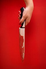 Close up of a female hand holds a bloodied knife. Red blood runs down it. Bright red background. Creep horror stories.