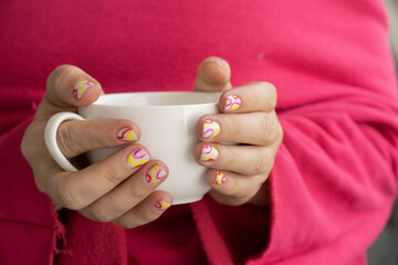Stylish colorful summer female nails holding white cup of coffee or tea. Modern trendy stylish Beautiful manicure. Cute pastel nail minimalistic design concept of beauty treatment. Gel nails. 
