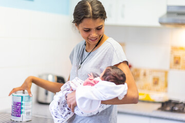 young teen girl holding her baby sister in kitchen with a can of infant formula on bench