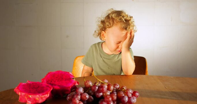 Young child sitting at a table with exotic fruits, striking dramatic and artistic poses, deep in imaginative play and contemplation. Portrait of an expressive toddler exploring his inner world.