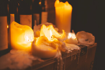 Closeup of large light color burning candles and dark glass wine bottles.