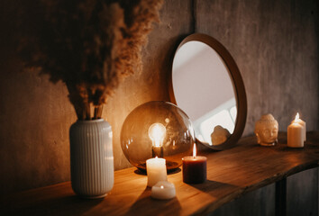 Round mirror on wooden shelf with two burning candles and small porcelain Buddha head