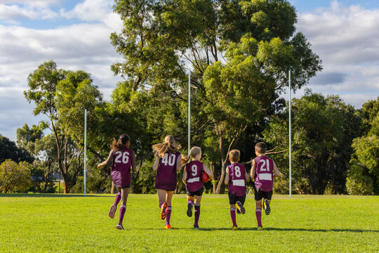 a group of kids running on a football oval seen from behind