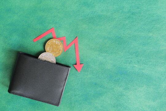 Human hand holding black a wallet with bitcoin and downward red arrow and coin inside. Cryptocurrency bear run and price decrease concept.