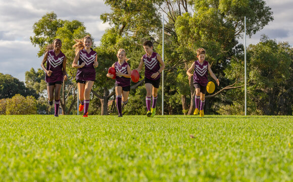 low angle image of children running on grass with afl footballs