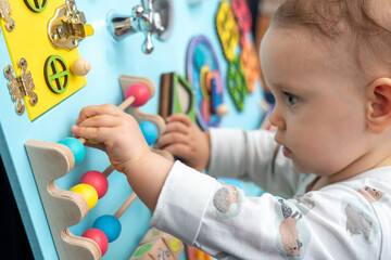 A baby moves round colored wooden elements on a busy board