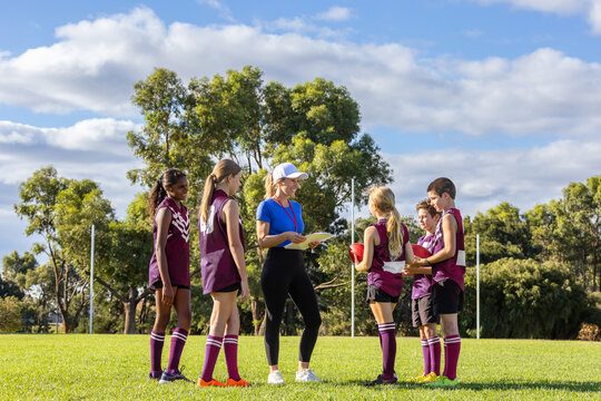 sports teacher addressing a group of children on football field