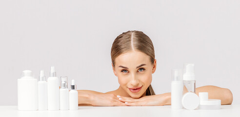 Nice woman on a white background among jars, bottles and tubes for cosmetic procedures. Production...
