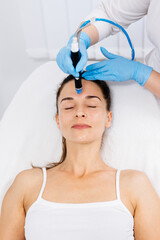 A cosmetologist wearing gloves performs vacuum cleaning and polishing of the facial skin of a...