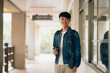 An Asian male student gazes into the camera, holding his course materials and carrying a backpack,...