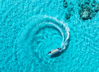 Aerial view of the speed boat in clear blue water on summer sunny day. Top drone view of fast floating yacht in ocean ocean. Travel in Maldives. Tropical landscape with motorboat on the sea. Travel