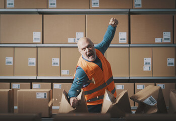 Furious rebellious worker tearing boxes at the warehouse - 784413549