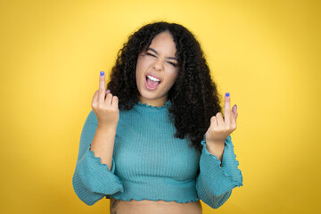 African american woman wearing casual sweater over yellow background showing middle finger doing...