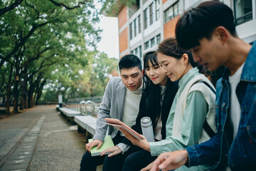 Asian university students sit in the campus, holding tablets, discussing their coursework. They use technology to experience modern learning methods.
