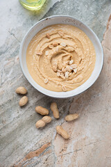 Bowl with peanut butter on a light-grey granite background, vertical shot with space, above view