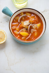 Turquoise serving bowl with manhattan clam chowder, vertical shot on a light-beige marble background with space, elevated view
