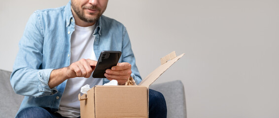 Man in a denim shirt unpacking package and takes a photo of his purchase, internet order. Person...