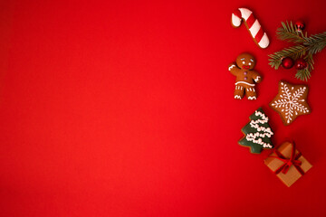 Cute red holiday background with cookies, sprig of fir tree with Christmas balls and a gift in craft paper. Cookies in the form of a gingerbread man, a Christmas tree, stars and a candy cone.