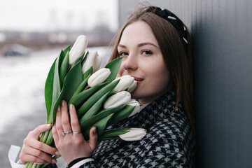 Young woman walking on the street with bouquet bunch of fresh spring tulips flowers, wind cold...
