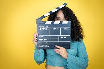 African american woman wearing casual sweater over yellow background holding clapperboard very...