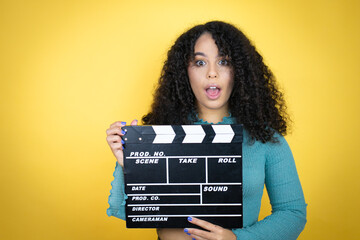 African american woman wearing casual sweater over yellow background holding clapperboard very...