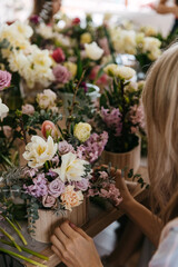 Over-the-shoulder view of a floristry session with hands arranging an intricate mix of pastel flowers in a wooden container.