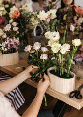 Close-up of a floral arrangement class, hands placing pale roses into a wooden pot.