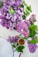 A bouquet of flowers on the window and coffee in a white cup in the rays of sunlight. A bouquet of lilacs and a cup of coffee. 
