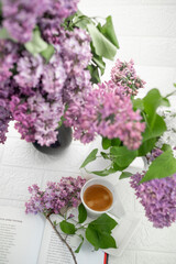A bouquet of flowers on the window and coffee in a white cup in the rays of sunlight. A bouquet of lilacs and a cup of coffee. 
