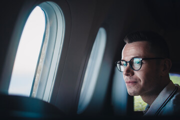 Portrait of successful man looking through window during flight. .