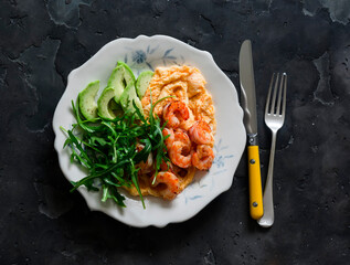 Delicious breakfast, brunch - omelette with shrimp, arugula and avocado on a dark background, top view