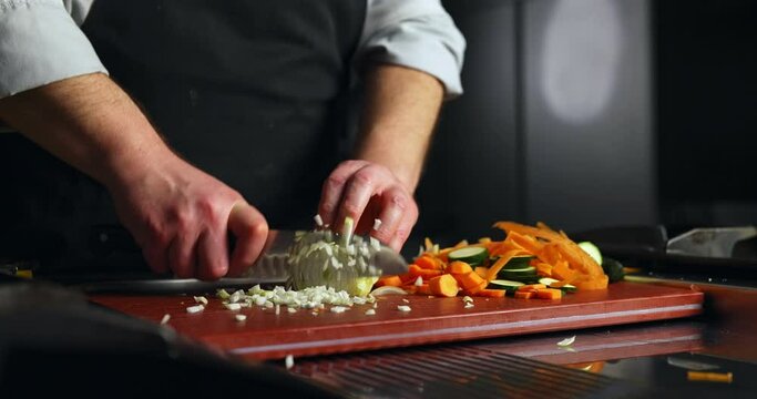 Professional Chef chopping green vegetables like carrots, zucchini and onion on a chopping board. Cook with sharp knife cutting veggies for fresh vegan or vegetarian meal.4K Slow motion footage.