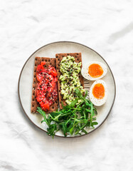 Rye crackers with avocado and salmon, boiled egg, arugula - delicious breakfast, snack on a light background, top view - 784473771