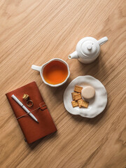 Tea break - cup of tea, dessert, leather notebook on a wooden background, top view