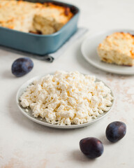 Plate of crumbly cottage cheese, plums, with a homemade casserole in the back.