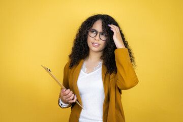 African american business woman with paperwork in hands over yellow background confuse and wonder about question. Uncertain with doubt, thinking with hand on head - obrazy, fototapety, plakaty