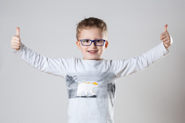 A young boy, wearing glasses, enthusiastically gives a thumbs up gesture